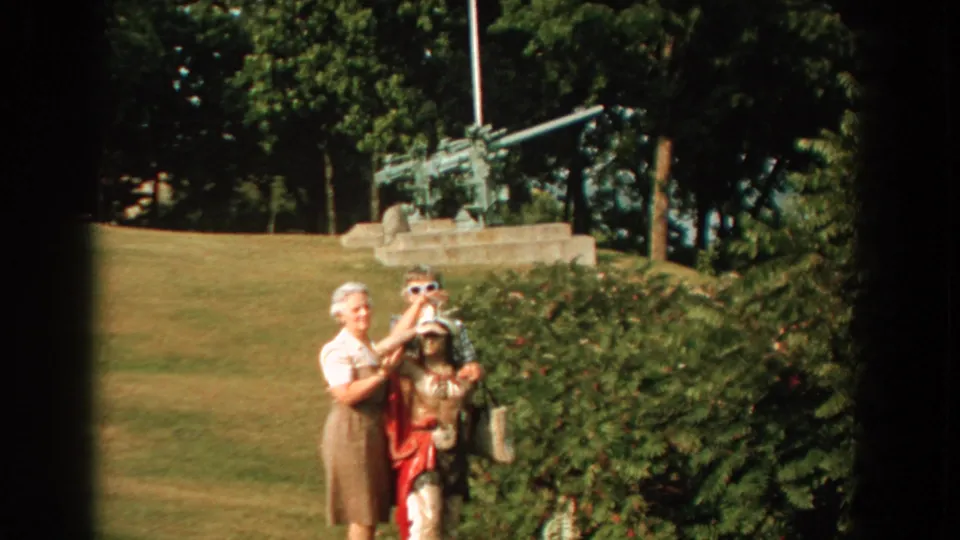 Two women and a child pose in a sunny Florida park, with one woman adjusting the child's hat and artillery visible in the background.