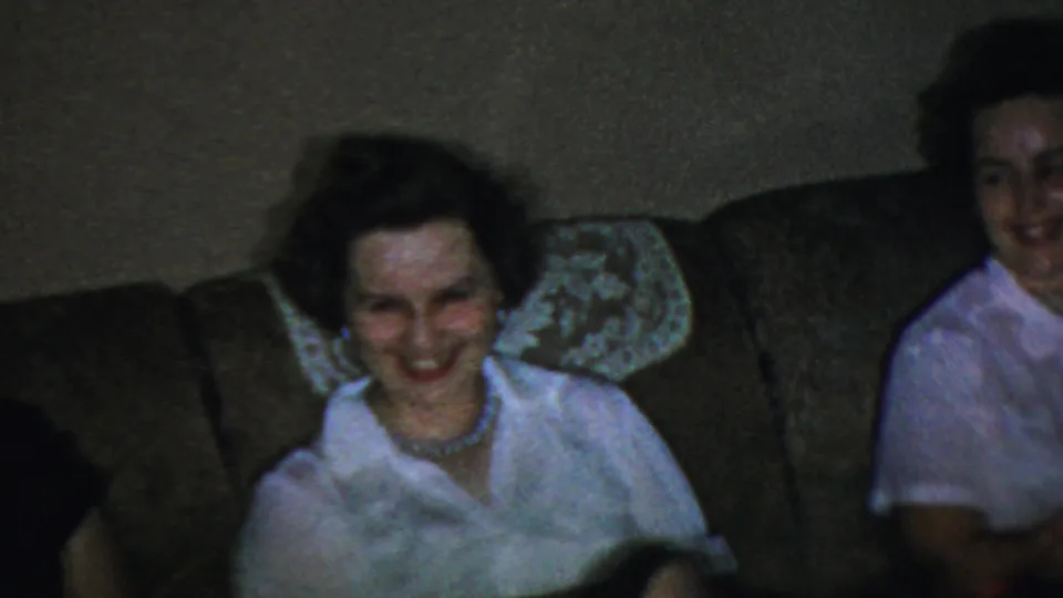The closing frame shows two adult women on a brown sofa in the supported Paramus 1959 home-movie interior, one smiling downward.