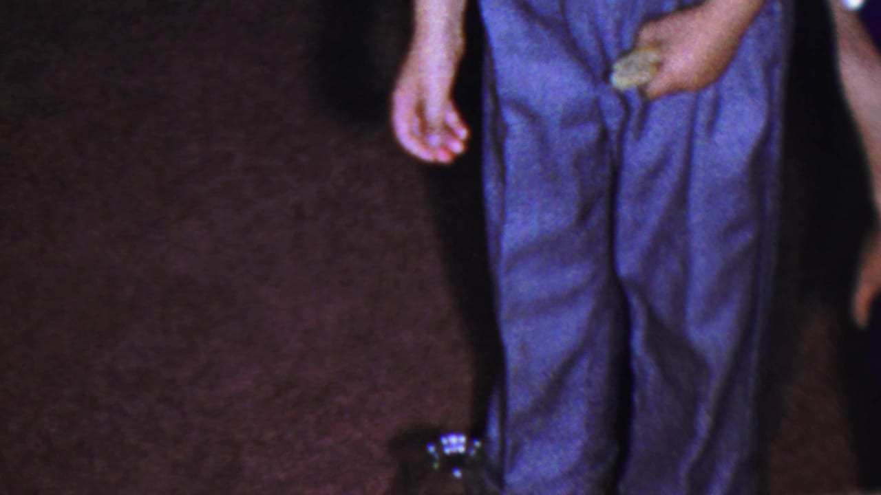 Cropped adults standing on maroon carpet near a dark glass jug.