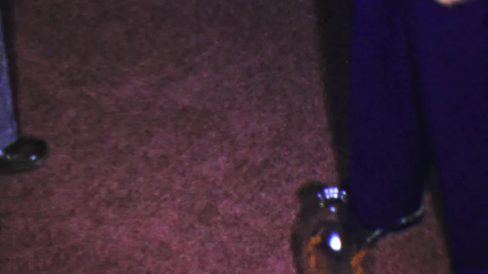 1959 Paramus frame focused on shoes, a dark glass jug, and textured maroon carpet inside a private home setting.