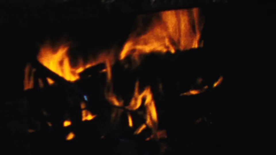 1959 Paramus home-movie frame of orange flames around logs in a dark fireplace, with strong contrast and warm 8mm color bloom.