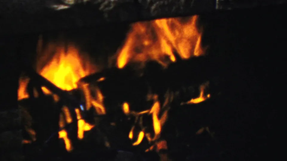 A late-1950s Paramus home-movie view of fireplace flames and logs, with bright orange highlights against a dark interior.