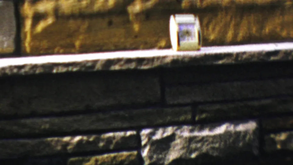 1959 Paramus home-movie frame showing a pale fireplace ledge, stone surround, and a small rectangular item near the hearth.