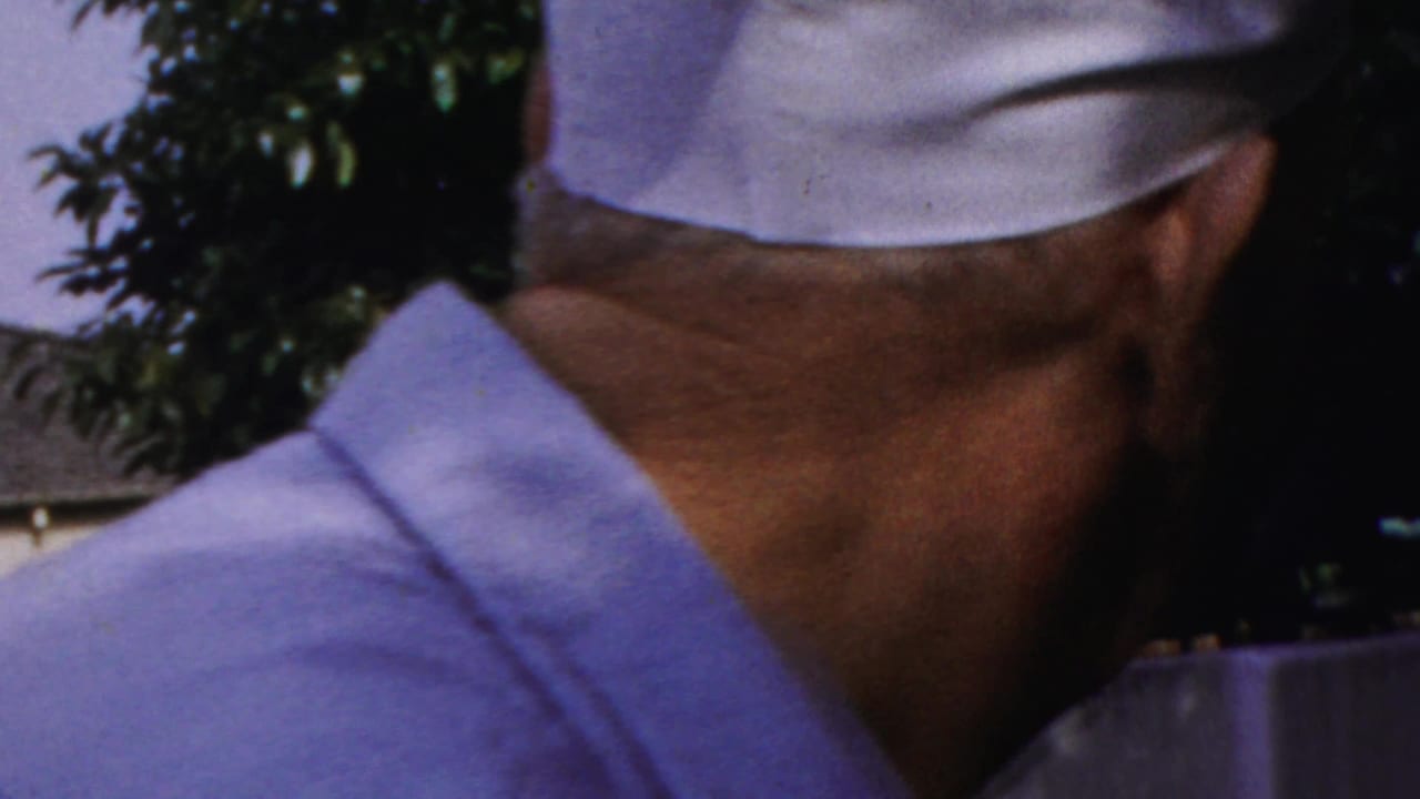 Older man in a white cap seen from behind beside another man outdoors.