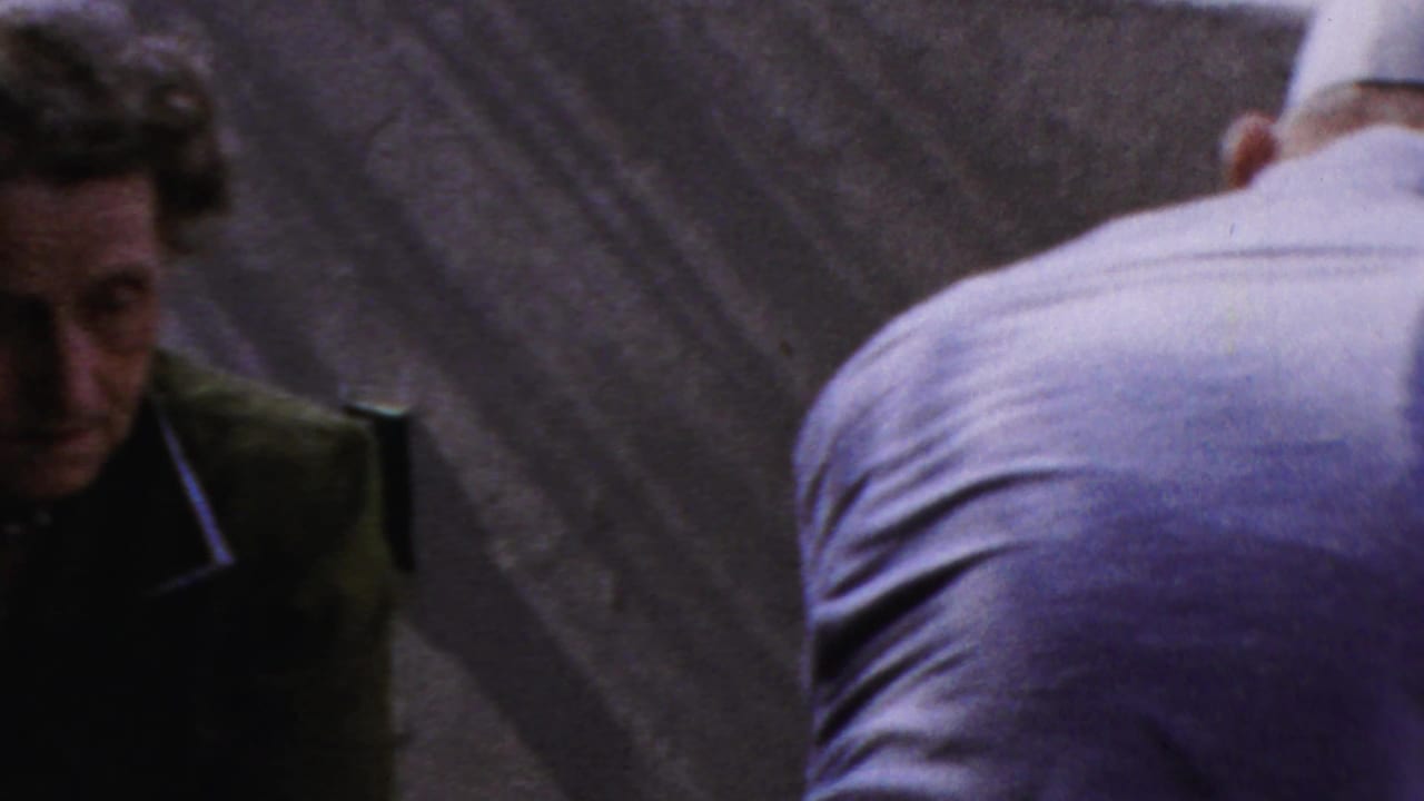 Woman in a green dress beside a blue-shirted person near a textured wall.