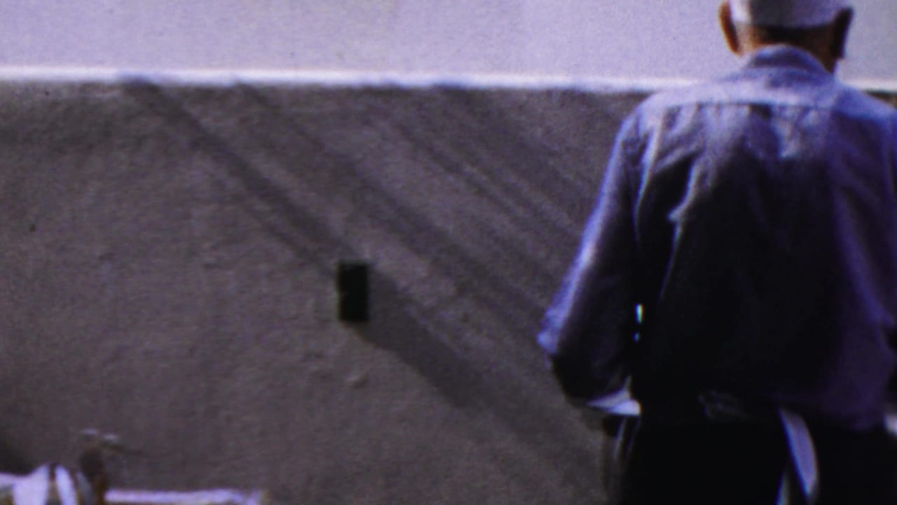 Waiter in a white cap and blue shirt seen from behind near a booth wall in the 1959 Paramus restaurant footage.