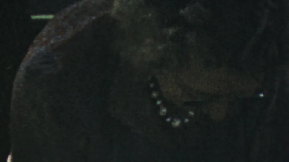 In 1959 Paramus home-movie footage, a woman wearing pearls sits close to the camera in shadow at an indoor gathering.