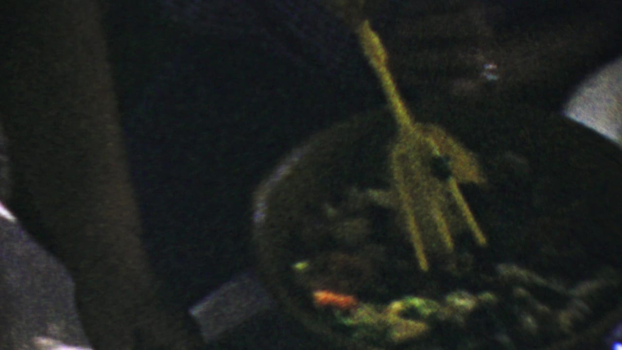A hand uses yellow serving tongs over salad greens in dim 1959 Paramus home-movie footage.