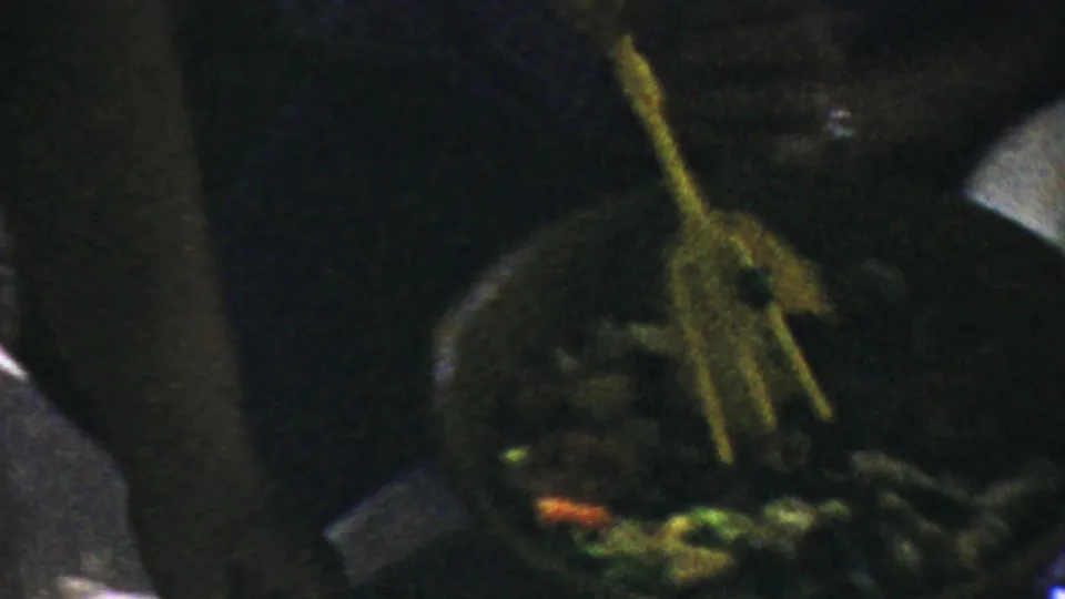 A hand uses yellow serving tongs over salad greens in dim 1959 Paramus home-movie footage.