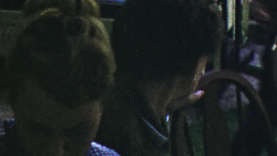 In 1959 Paramus home-movie footage, two women sit close together in a dark shaded structure, with faces only partly visible.