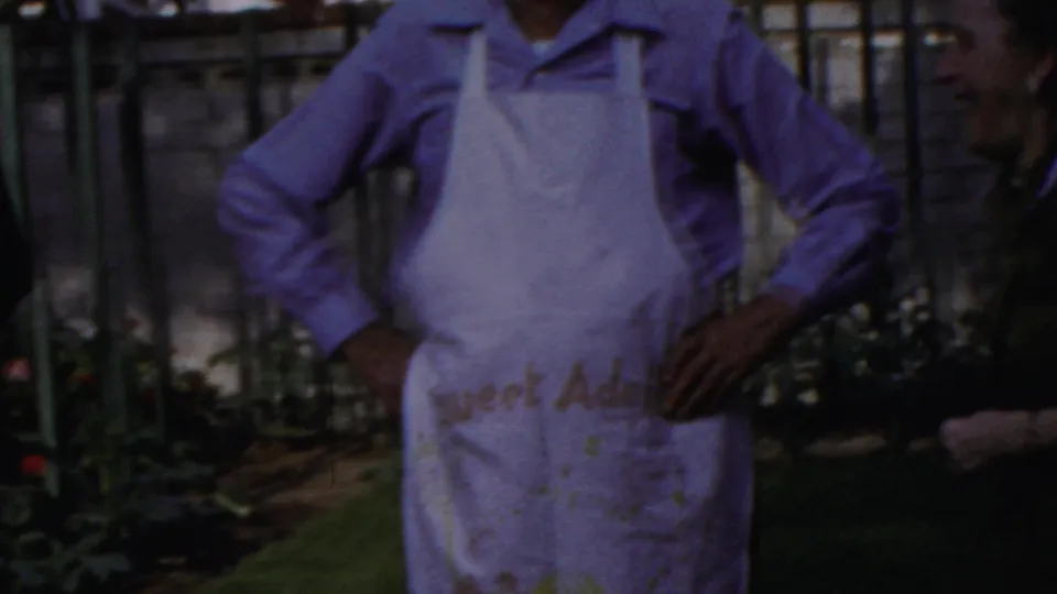 1959 Paramus frame showing a man in a chef hat and stained apron standing proudly in a backyard barbecue setting.
