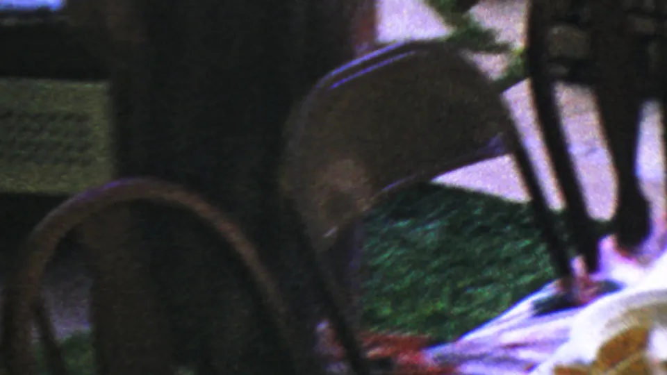 1959 Paramus home-movie frame with wooden chairs, grass, and part of a table setting at the edge of the shot.