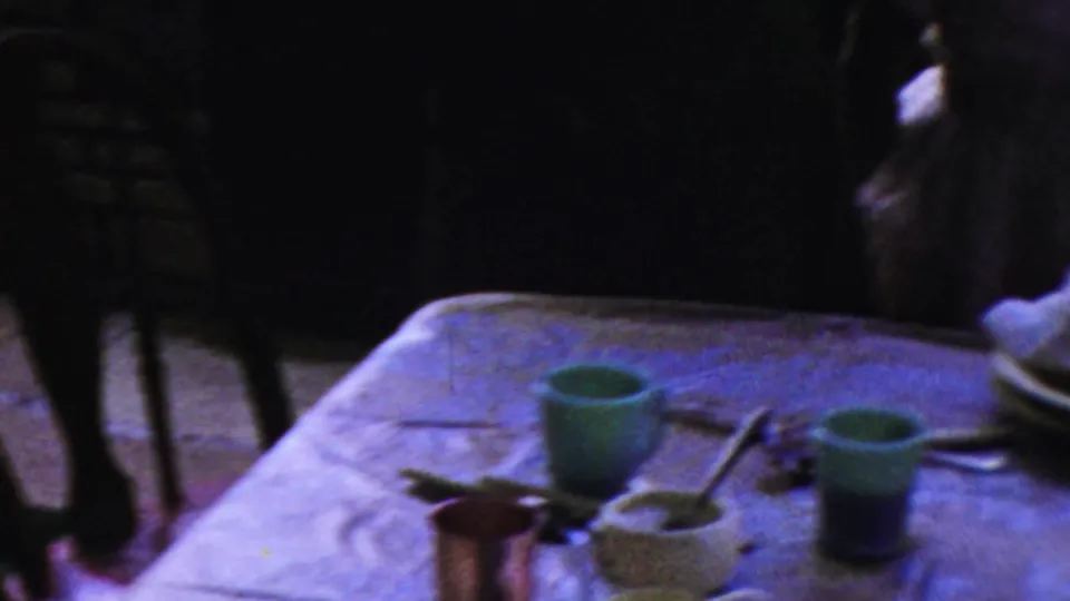 1959 Paramus home-movie frame showing a table with green cups, utensils, plates, and people partly visible beyond it.