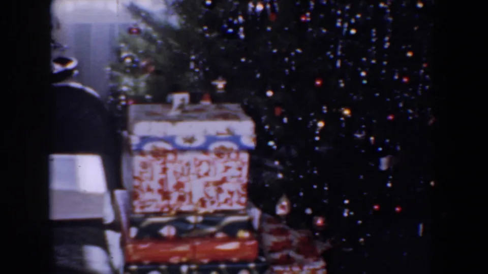1960 Bel Air, Maryland 8mm frame with a decorated Christmas tree, stacked presents, and a nearby lamp in soft focus.