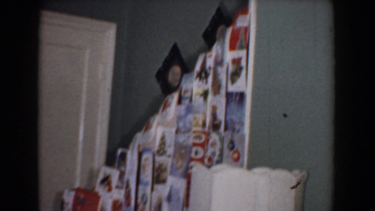 1960 Bel Air, Maryland home-movie frame showing wrapped Christmas presents near a white interior door, cream lamp shade, and muted green wall.