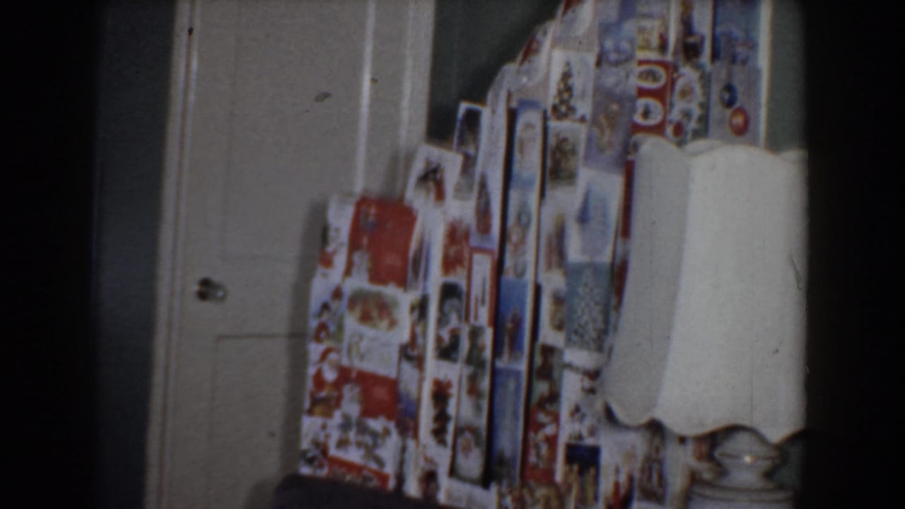 Wrapped holiday presents stacked near a closed door with a lamp at right.