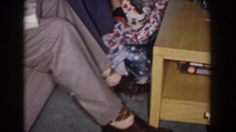 The frame shows seated guests' legs, holiday packages, and a small table within the Bel Air living-room gathering.