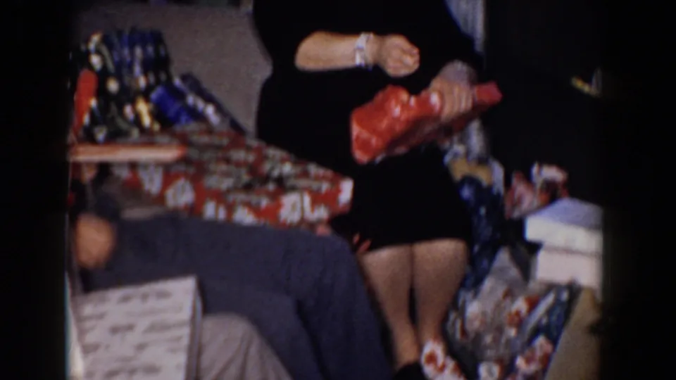 The woman continues tearing into the red present in a 1960s Bel Air home interior with packages nearby.