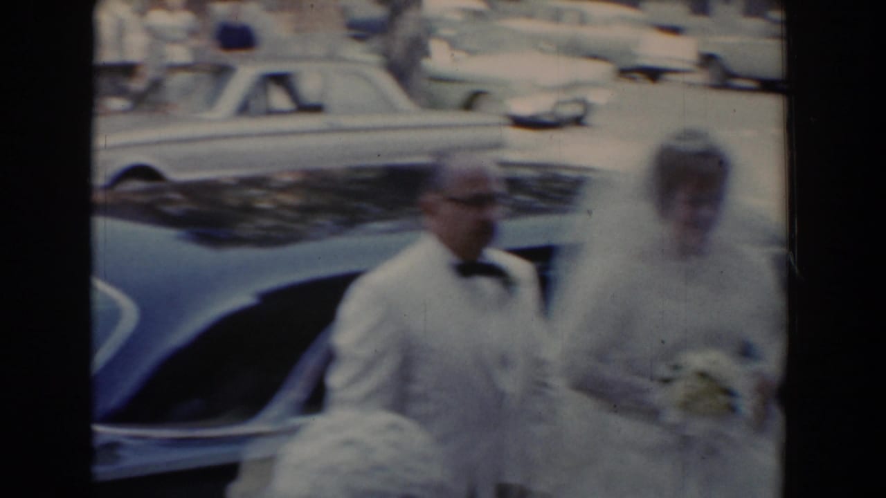 In Bel Air, Maryland in 1960, a bride in a white veil stands with her father in a white tuxedo beside a parked car.