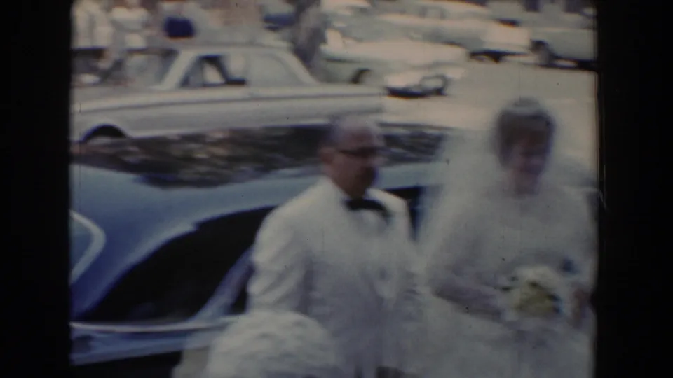 In Bel Air, Maryland in 1960, a bride in a white veil stands with her father in a white tuxedo beside a parked car.