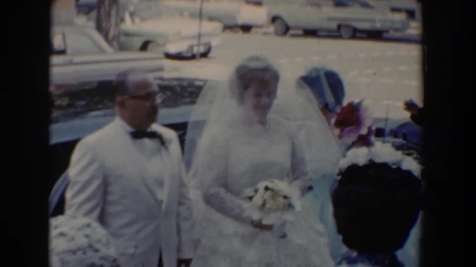 The bride and her father pose near a bridesmaid in blue, with mid-century cars visible in the Bel Air parking area.