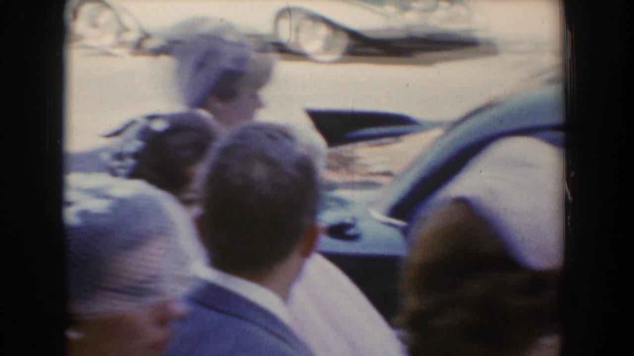 In Bel Air, Maryland in 1960, guests in formal attire crowd around a car as the bride approaches or exits nearby.