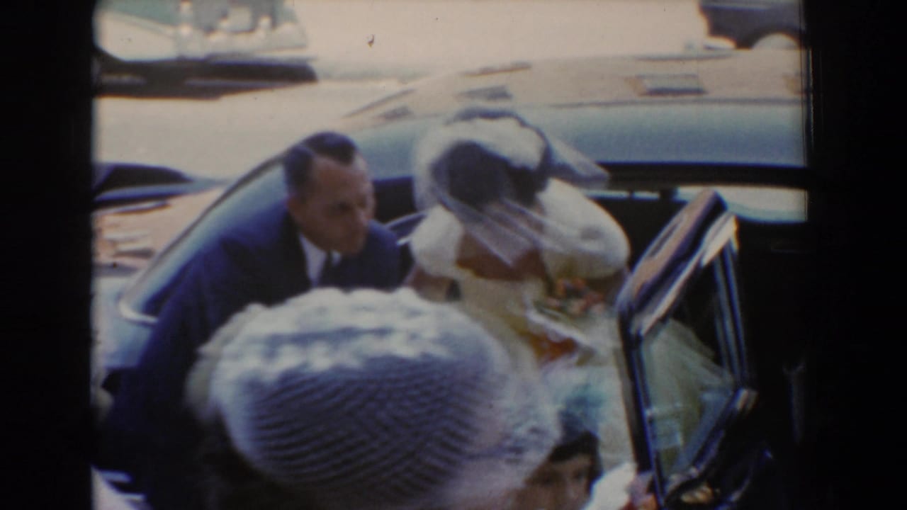 A man in a dark suit assists a bride beside an open car door.