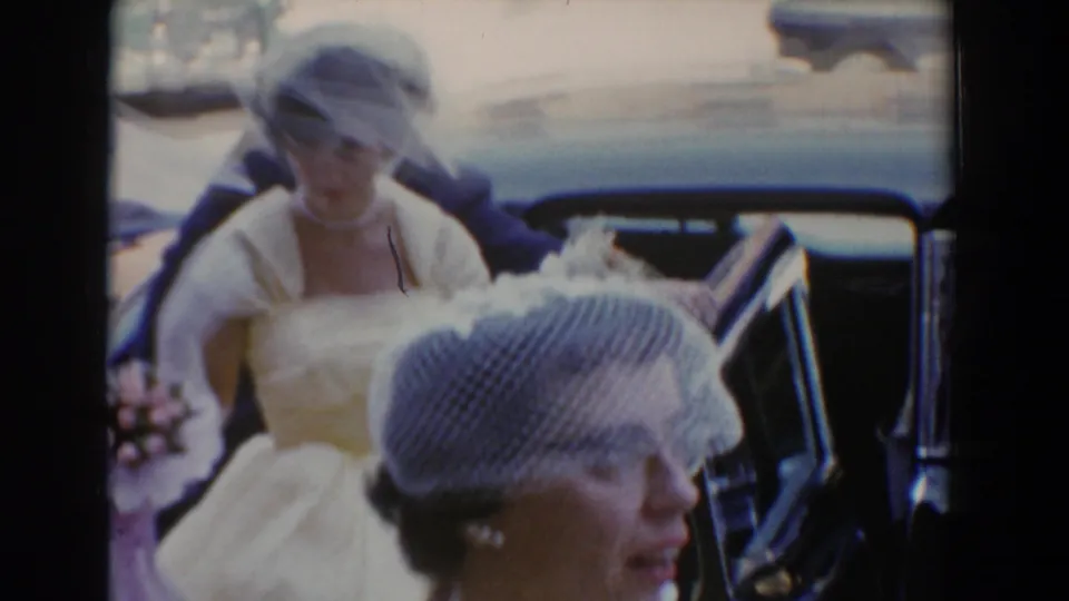The bride steps forward through a close group of wedding guests in veiled hats and formal clothing in Bel Air, Maryland.