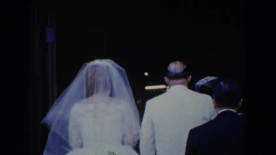 1960 Bel Air, Maryland home-movie frame showing a bride in a veil walking with a man in a light suit during a wedding procession.