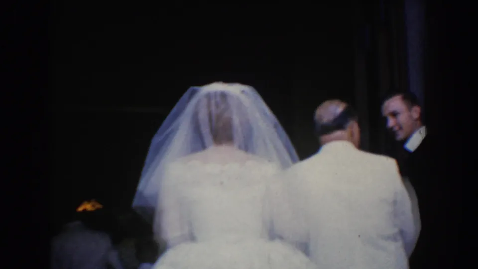 The bride and her father are seen from behind in a dim interior, with suited men waiting near the doorway in this 1960 Maryland wedding footage.