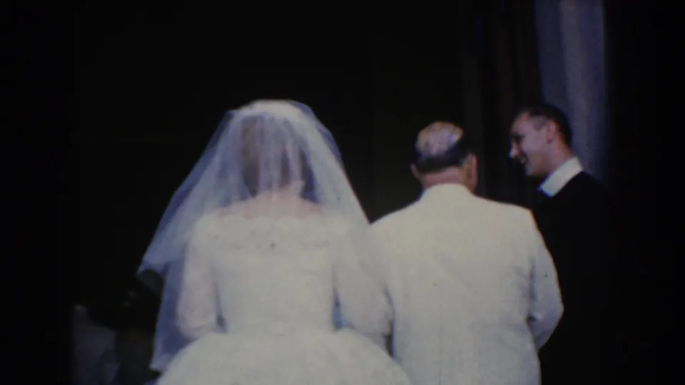 The bride and her father move together toward the dark doorway, with two suited men visible to the side in the 1960 Bel Air wedding scene.