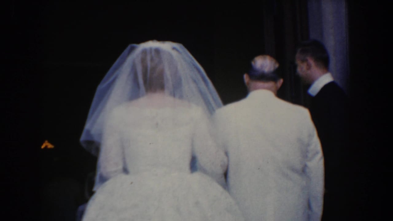 Bride in veil walks beside a man in a light suit at a dark church doorway.