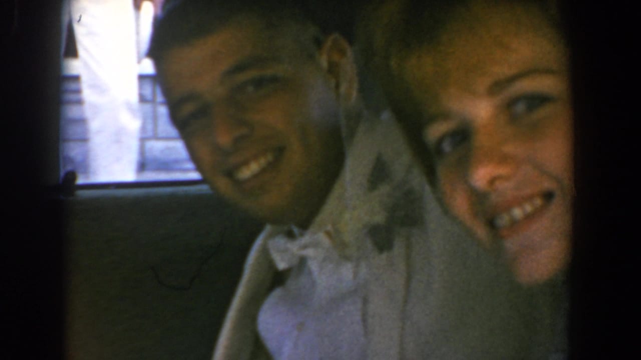 Young couple in formal attire smiles through an open car window.