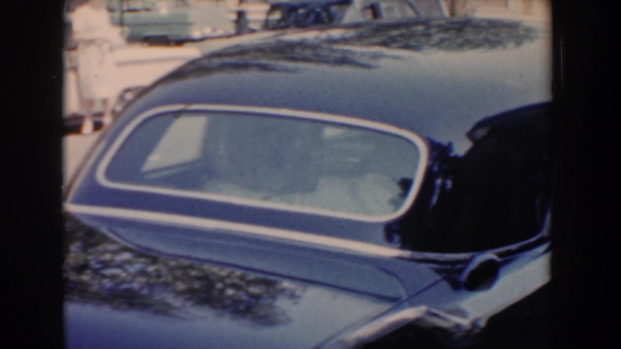 Black vintage car viewed close up through its rear side window, with other parked cars behind it.