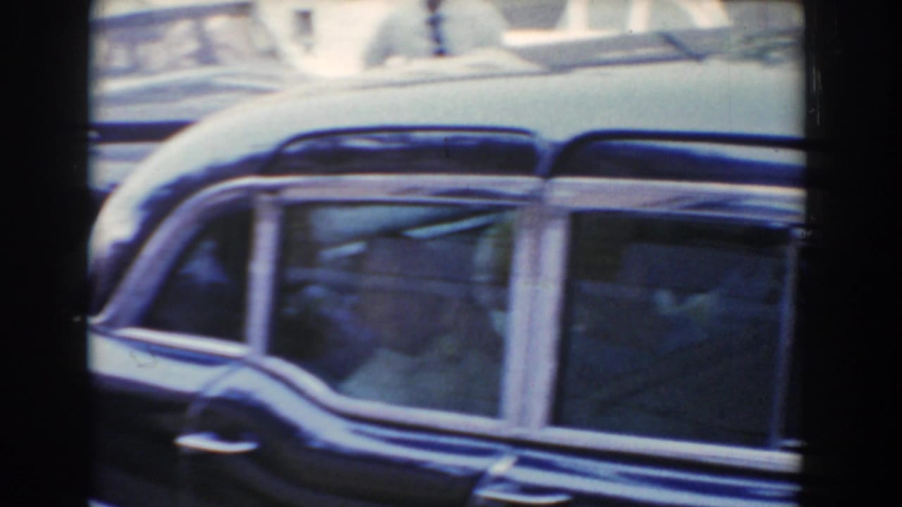 Side view of a dark vintage car with passengers behind glass.