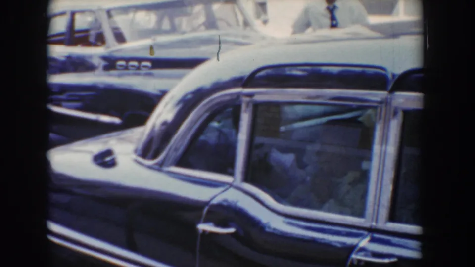 Close 8mm view of a dark station wagon in 1960 Bel Air, Maryland, with other automobiles packed nearby.