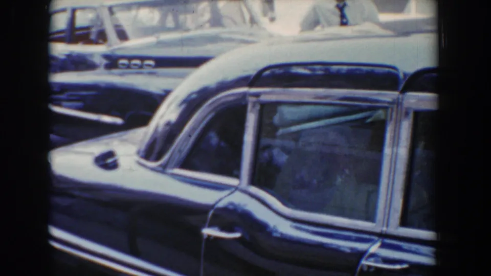 A dark vintage car passes slowly through Bel Air, Maryland traffic, with soft 8mm color and gate borders visible.