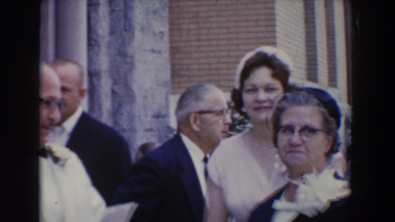 Formally dressed adults stand outside a stone and brick building.