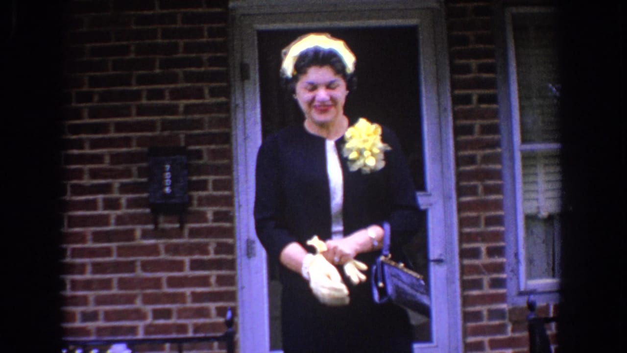 In Bel Air, Maryland circa 1960, a woman in formal dress stands outside a brick home with white gloves and a yellow corsage.