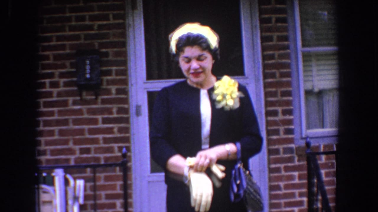 Woman looks down while adjusting white gloves outside a brick doorway.