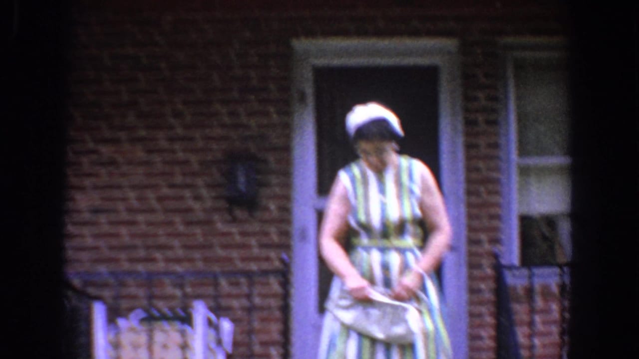 Woman steps out from a brick home doorway while holding a light handbag.