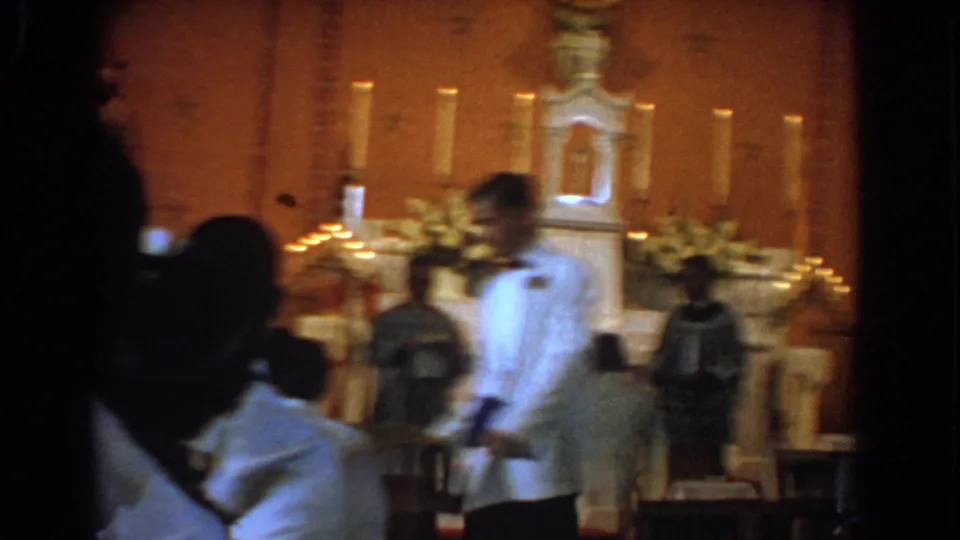 A motion-blurred 8mm frame captures the man passing the pews in front of the candlelit altar in Bel Air, Maryland.