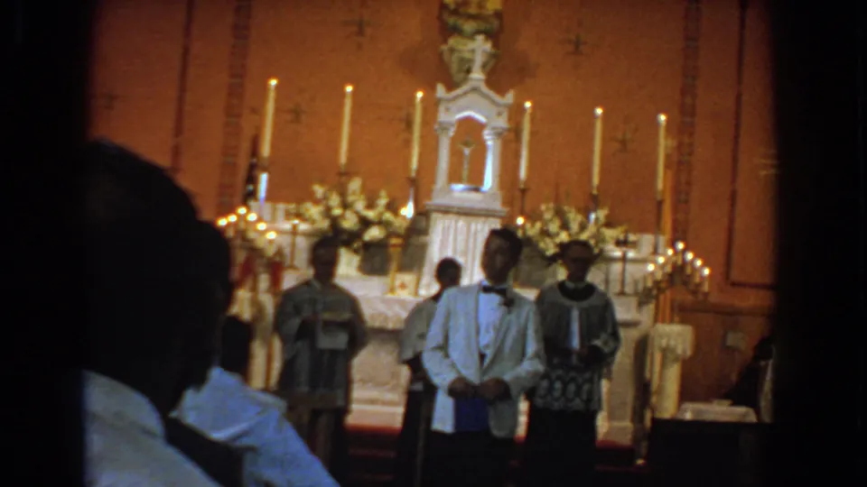 Bel Air, Maryland 1960 church ceremony frame with the young man standing before a decorated altar and vested clergy.