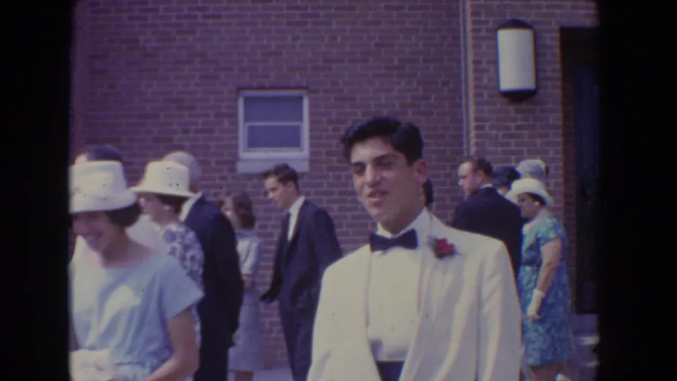 Groom in white formalwear stands outside the Bel Air church while wedding guests pass nearby.