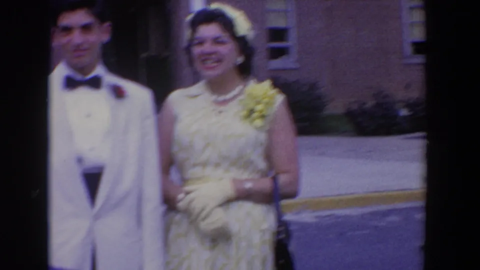 In Bel Air, Maryland, 1960, a man in formal wear and a woman with corsage and hat stand outside a brick building.