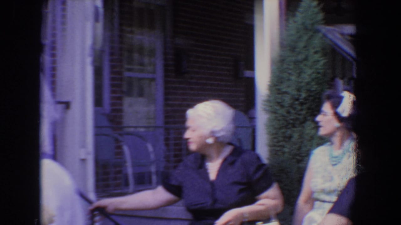 Adults in formal clothing stand near a brick residential porch in bright sunlight.