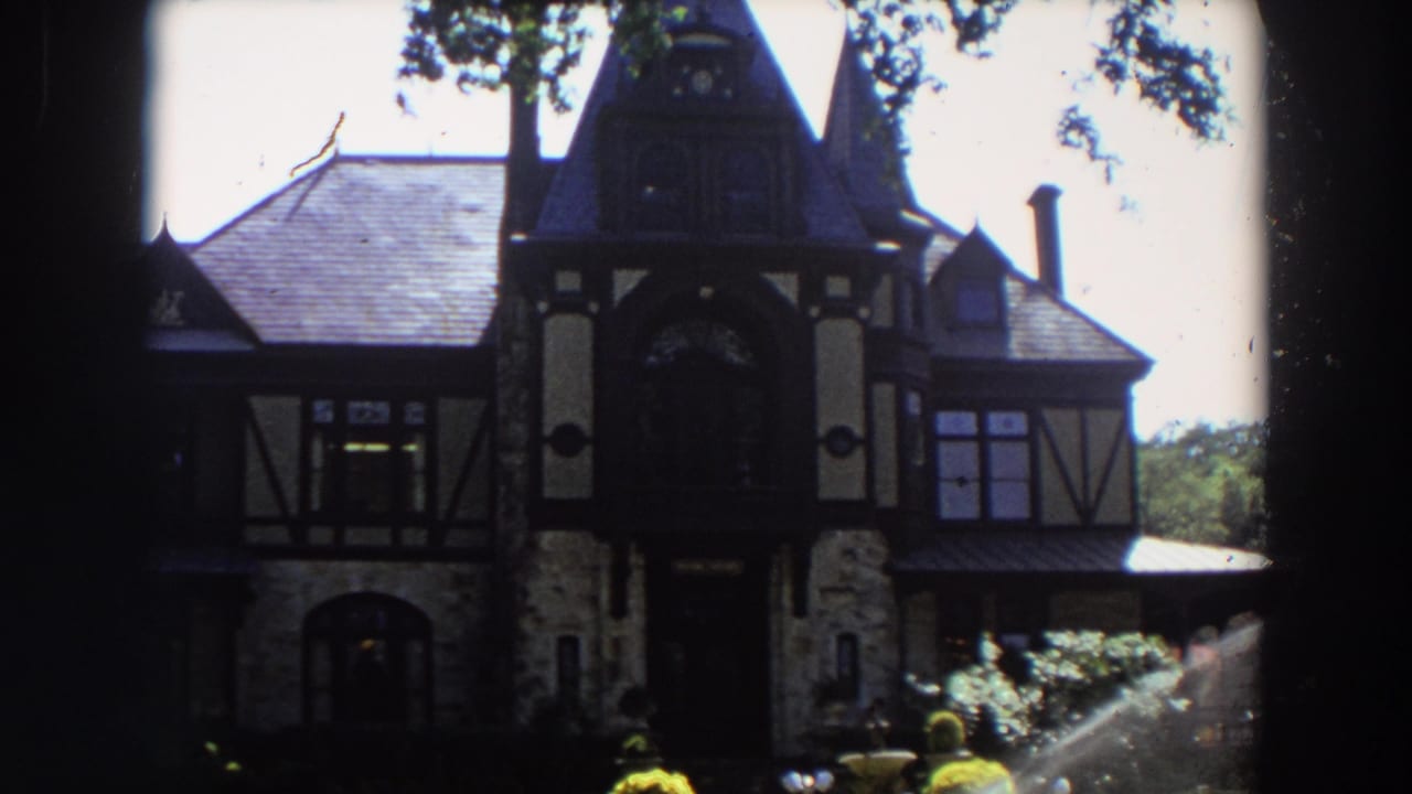 Tudor-style house partly shaded with a sprinkler spraying in the foreground garden.