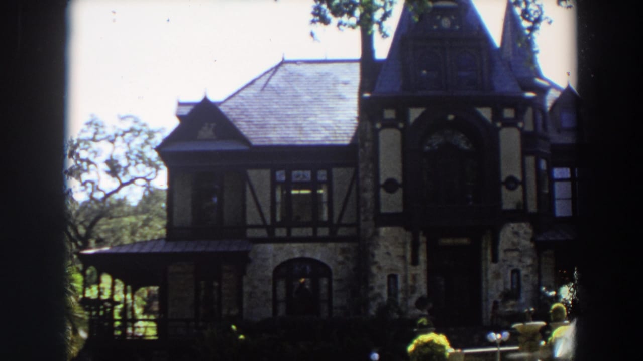 Large stone-and-timber house with steep roof and tower seen through dark foreground edges.