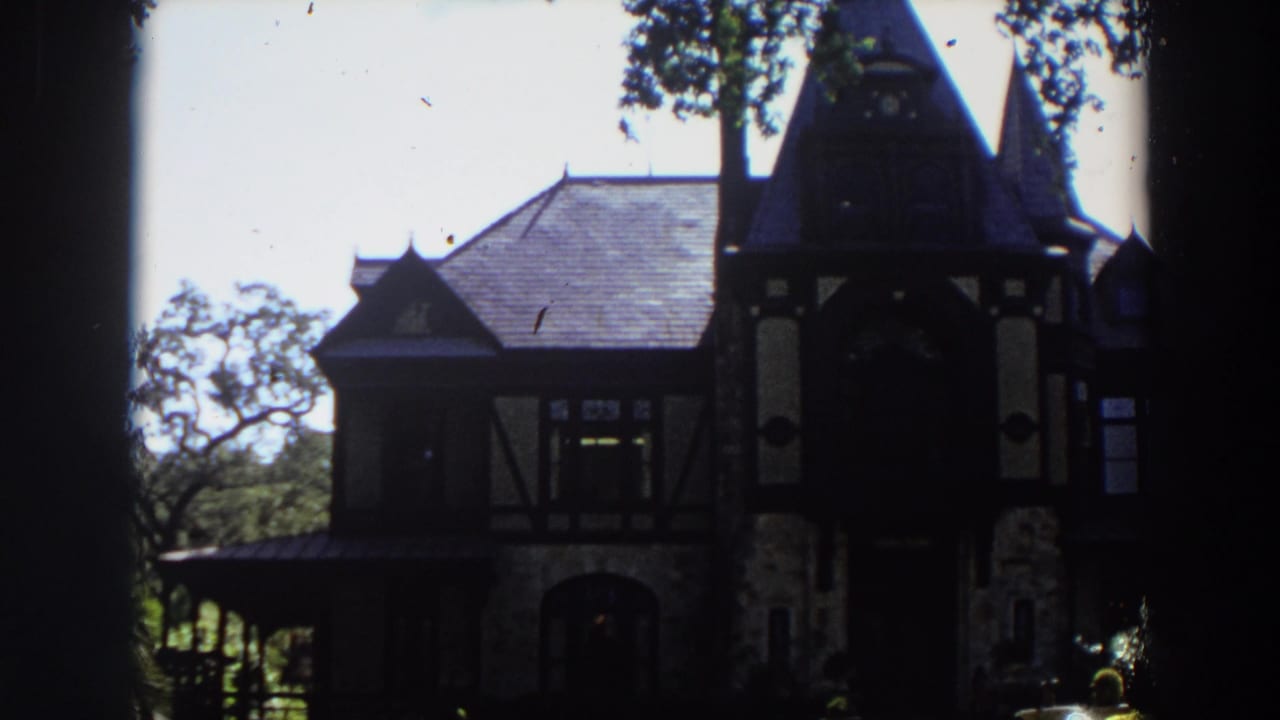 Old house exterior with tower, steep roof, trees, and shaded porch area.