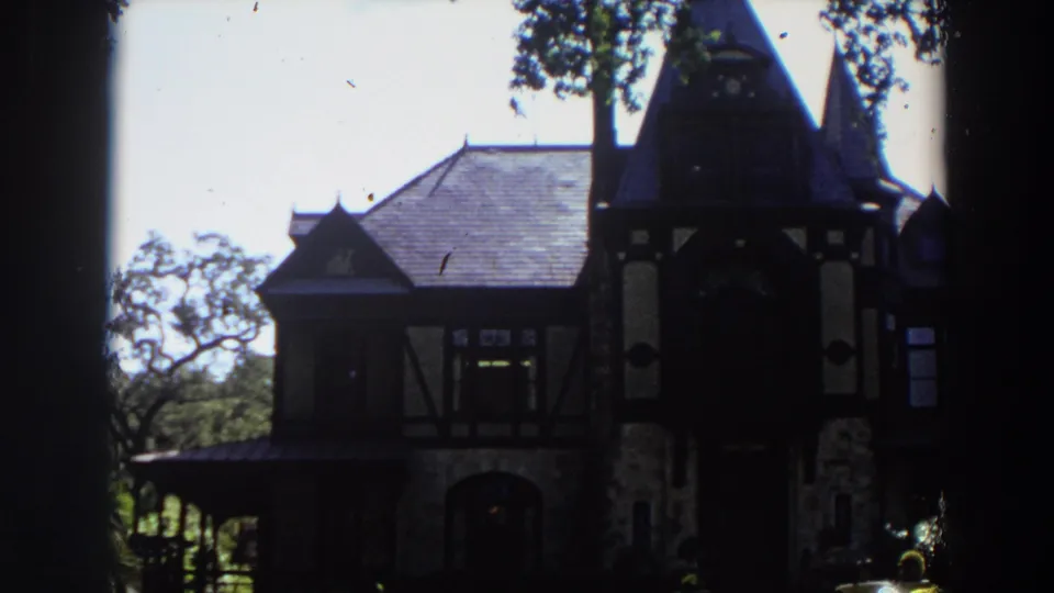 1964 California home-movie view of a large old house with tower rooflines, timber framing, and surrounding trees.